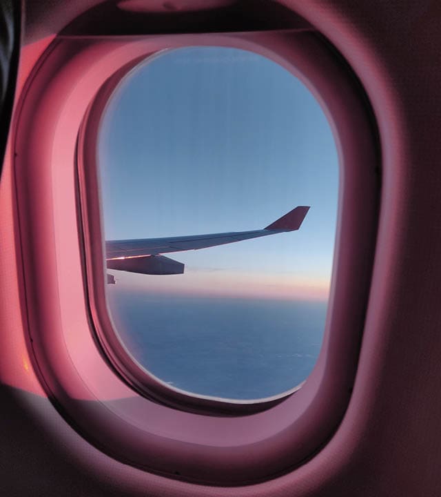 The window and the wing of a plane glows golden as it is flying at sunset