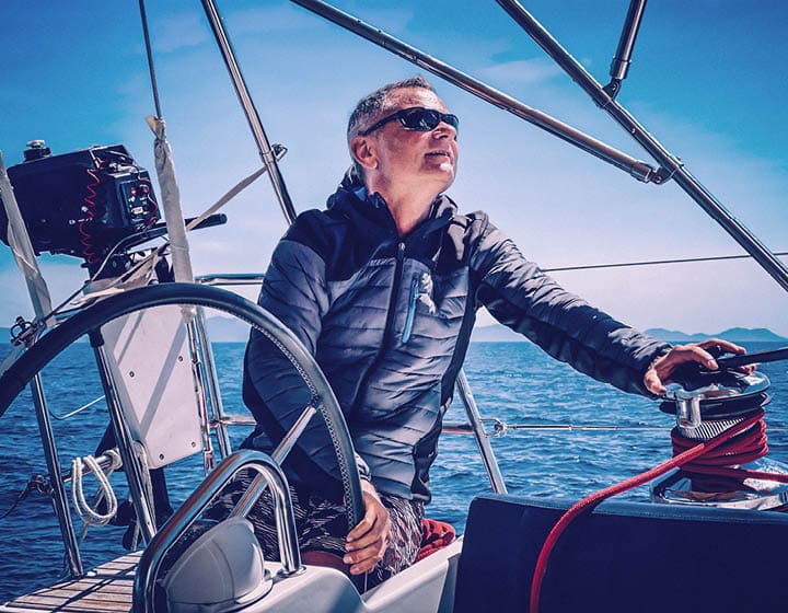 Skipper driving sailboat holding steering wheel.
