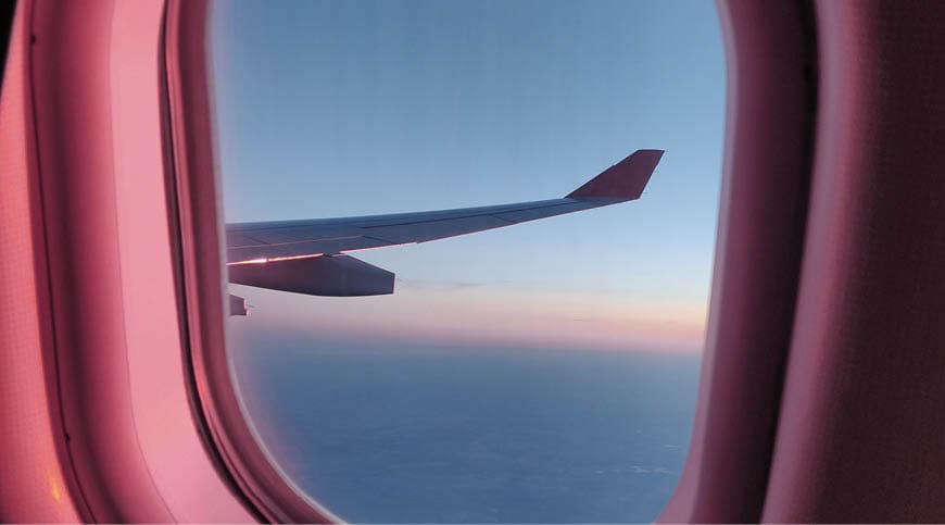 The window and the wing of a plane glows golden as it is flying at sunset