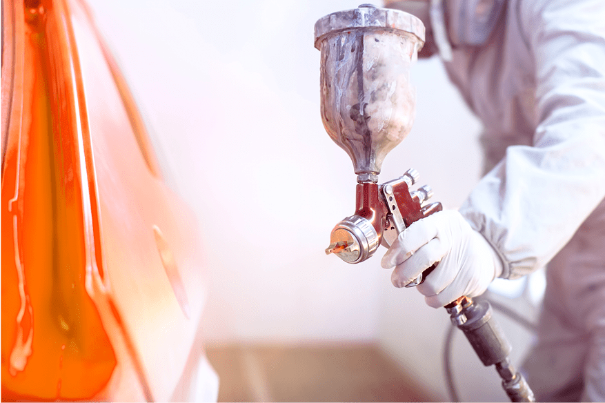 Close-up of spray gun with red paint painting a car in special booth