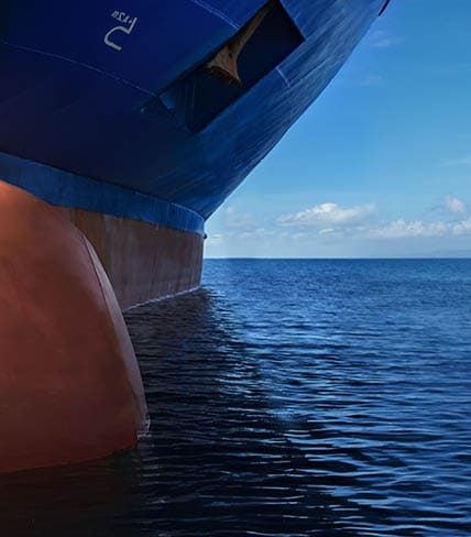 Close up of large blue merchant crago ship in the middle of the ocean underway. Performing cargo export and import operations with sun rays, horizon line and beautiful sky.